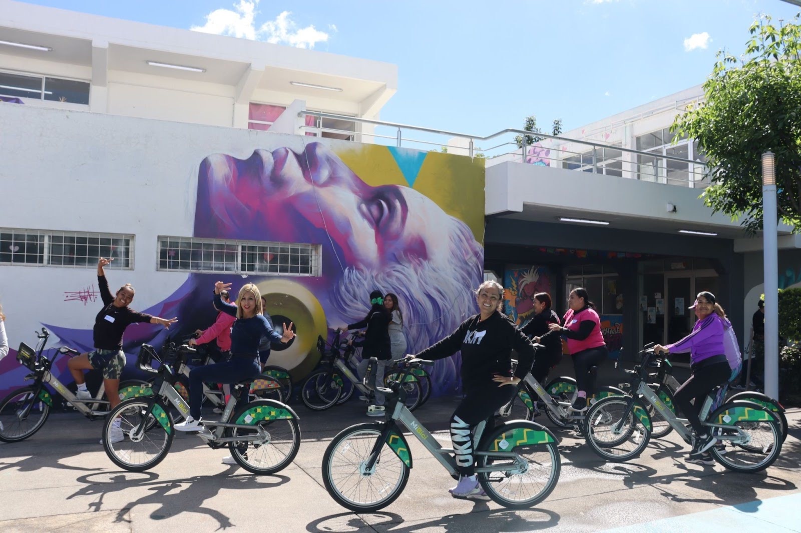 Women riders on MiBici bikes in front of a large mural in Guadalajara